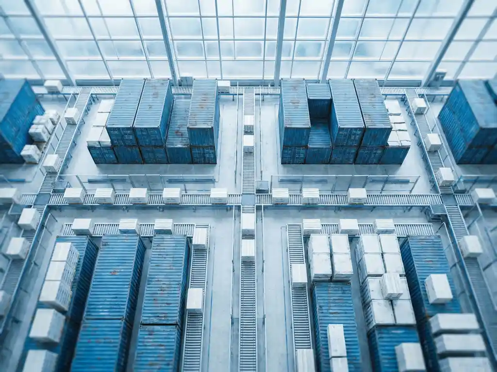 Aerial view of a vast logistics hub with interconnected shipping containers, cargo pallets, and conveyor paths in cool blue and white tones.